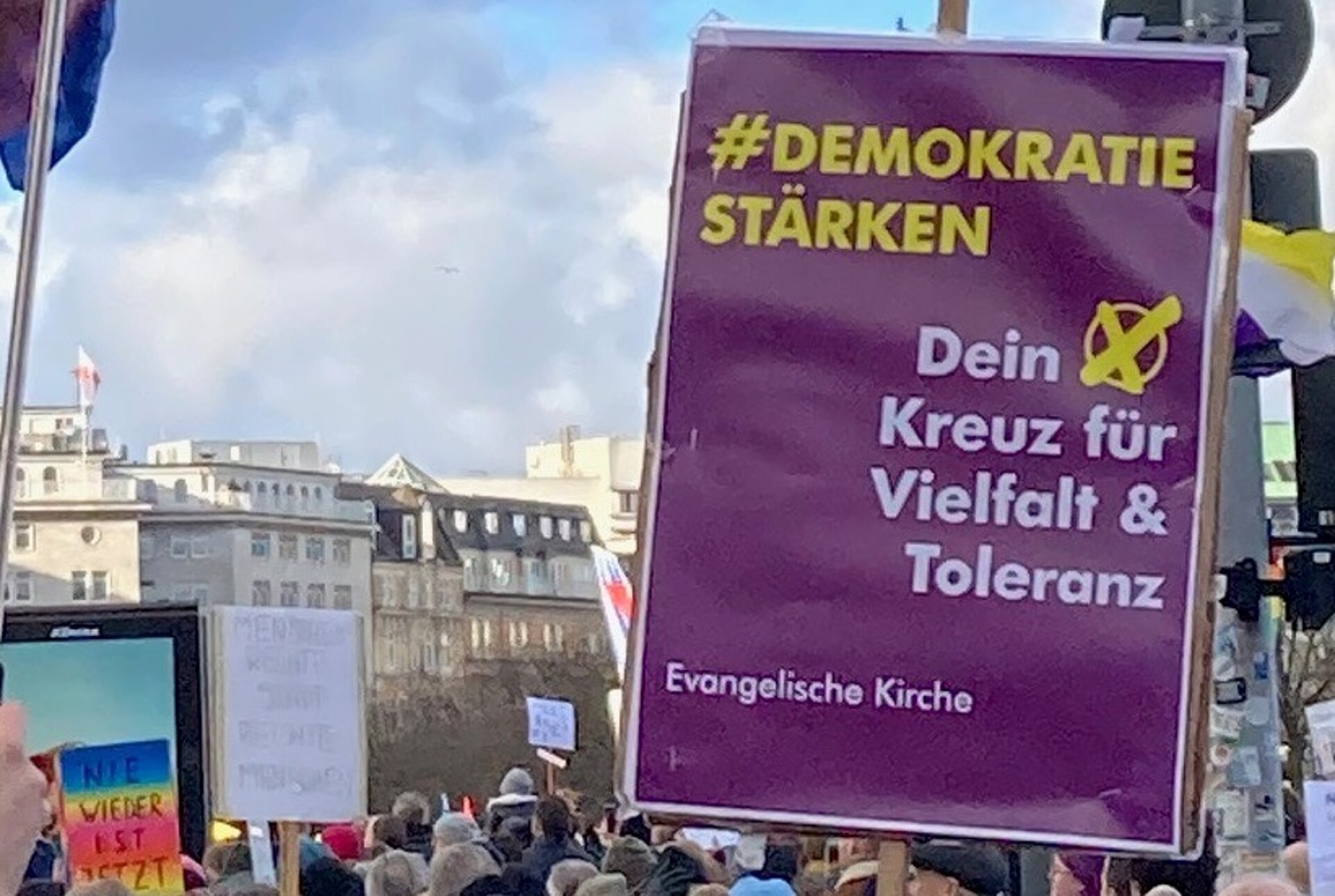 Foto eines Plakates auf einer Demonstration mit dem Titel "Demokratie stärken" und dem Text "Dein Kreuz für Vielfalt und Toleranz" 
